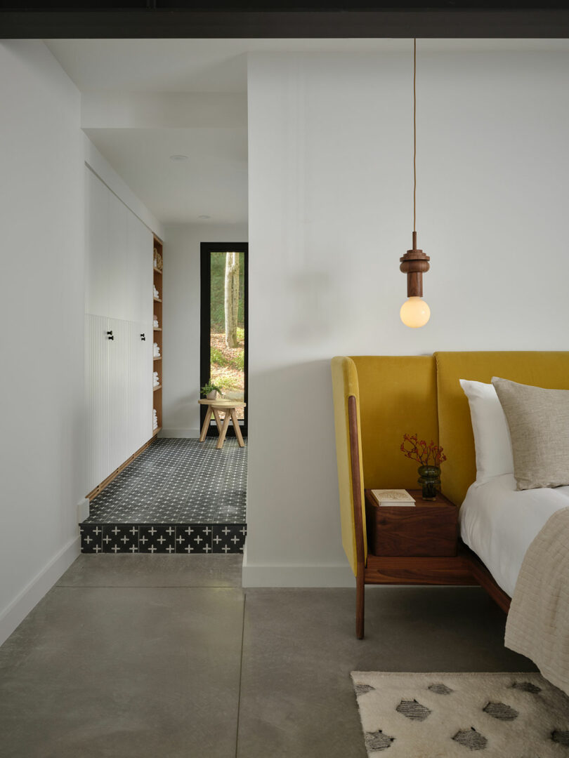 A modern bedroom with a yellow bed frame and a view through a doorway to a patterned tile hallway.