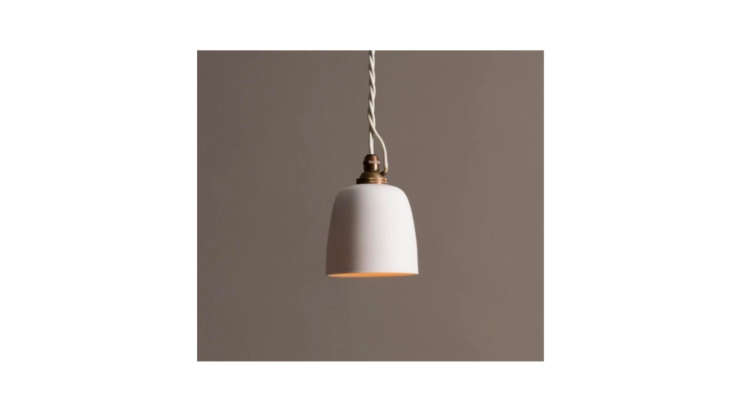 A small porcelain beaker-style pendant light hanging near the bedside.