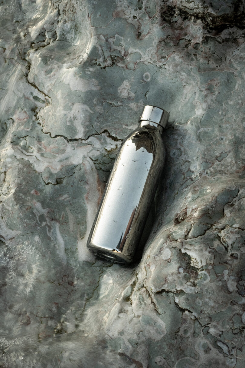 A stainless steel Aarke To-Go Bottle resting on a rough, textured stone surface.