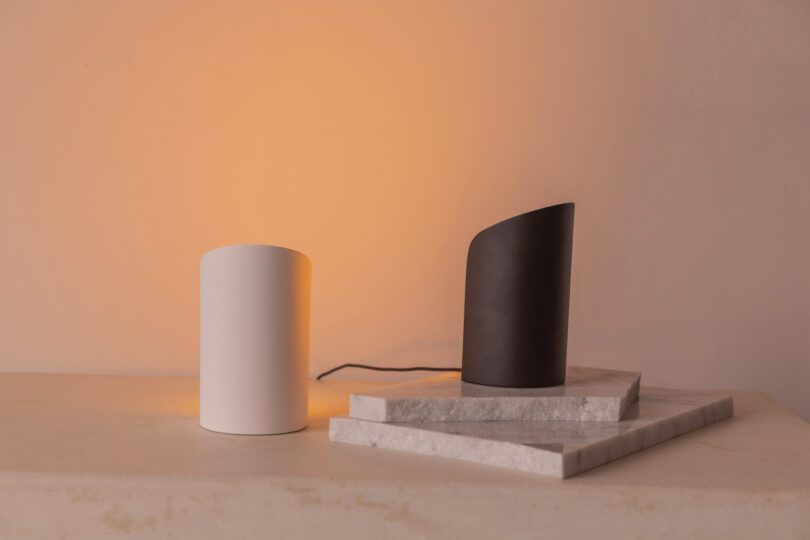 Black and white Philips Hue cylindrical light units placed on modern marble slabs.