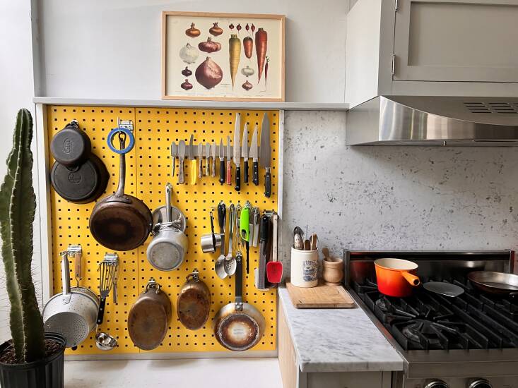 Close-up of a powder-coated steel pegboard holding various stainless steel pans, utensils, and kitchen tools.