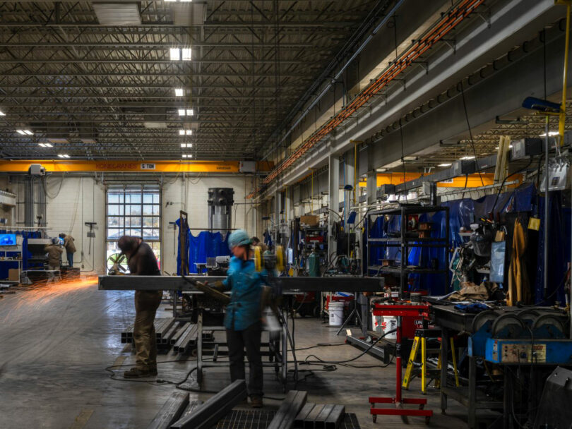 Workers welding steel beams in an illuminated industrial workshop designed with architectural precision.