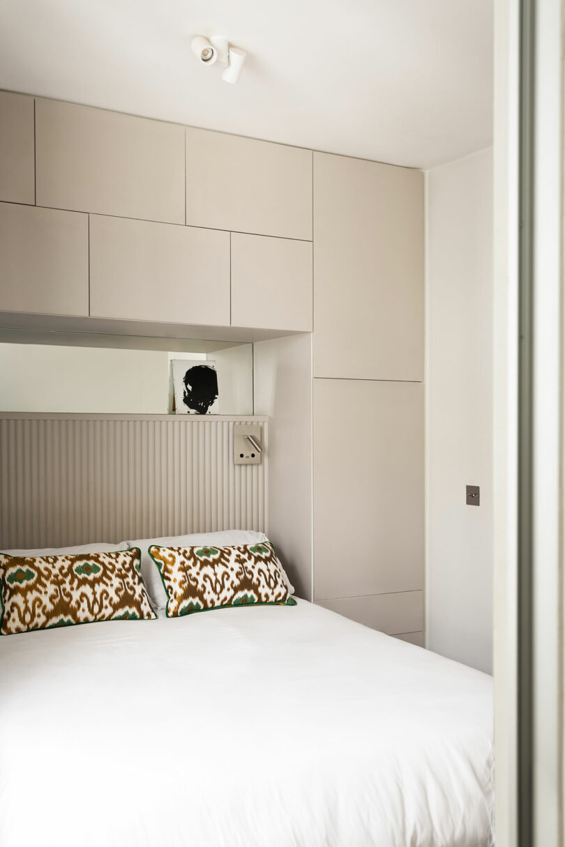 A minimalist bedroom featuring integrated beige storage units and a monochrome artwork above the bed.