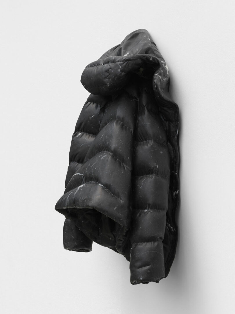 A hyper-realistic marble sculpture of a puffer jacket rendered in dark stone.