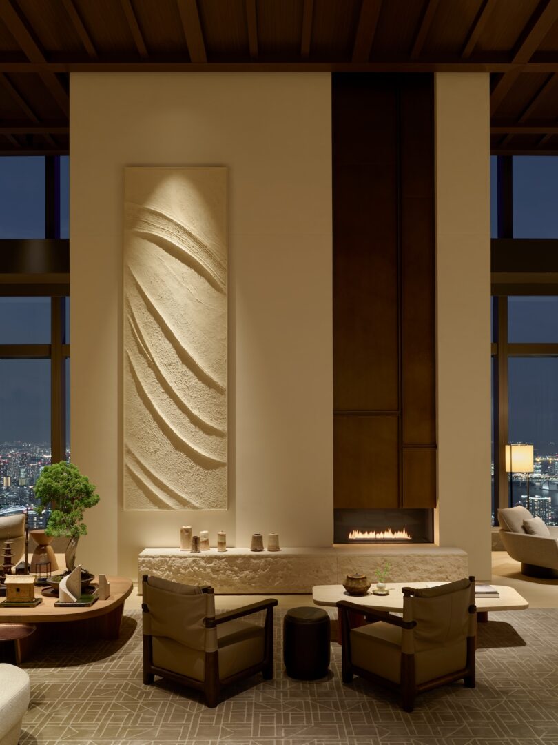 Modern interior with a lit fireplace, textured walls, and a view of the city lights through a large window.