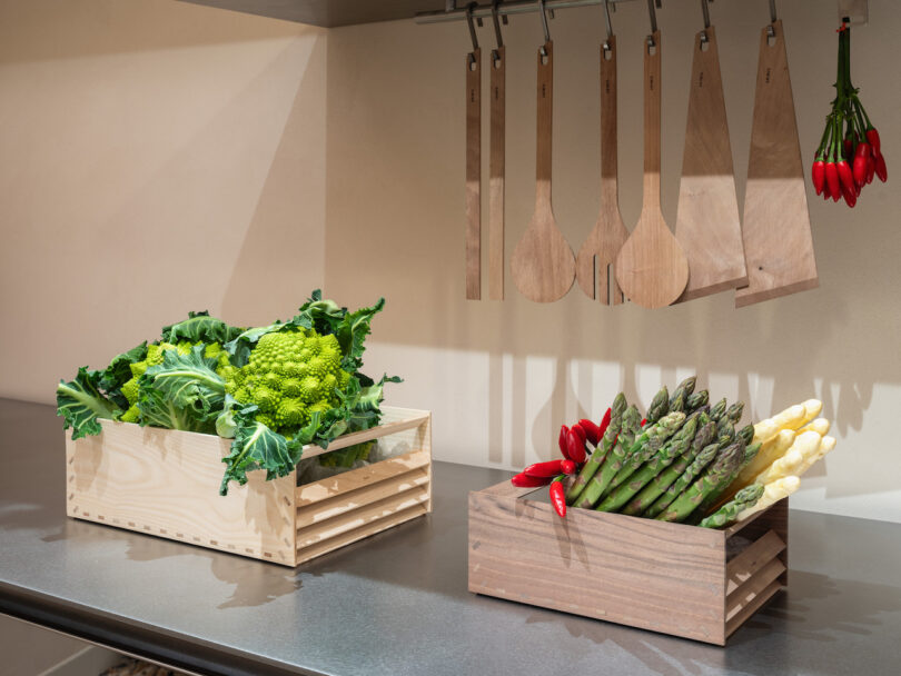 Two wooden crates filled with fresh vegetables on a kitchen counter.