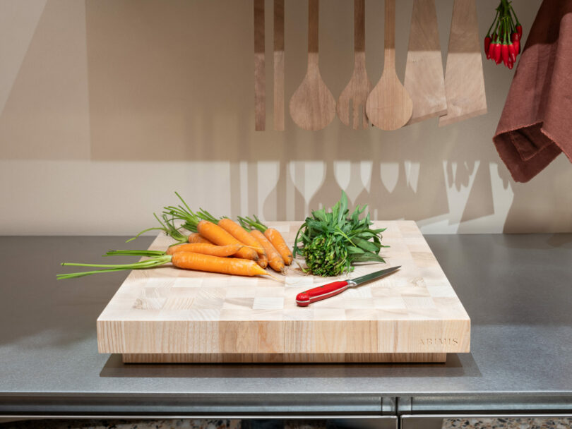 Wooden cutting board with carrots and a knife on a stainless steel counter.