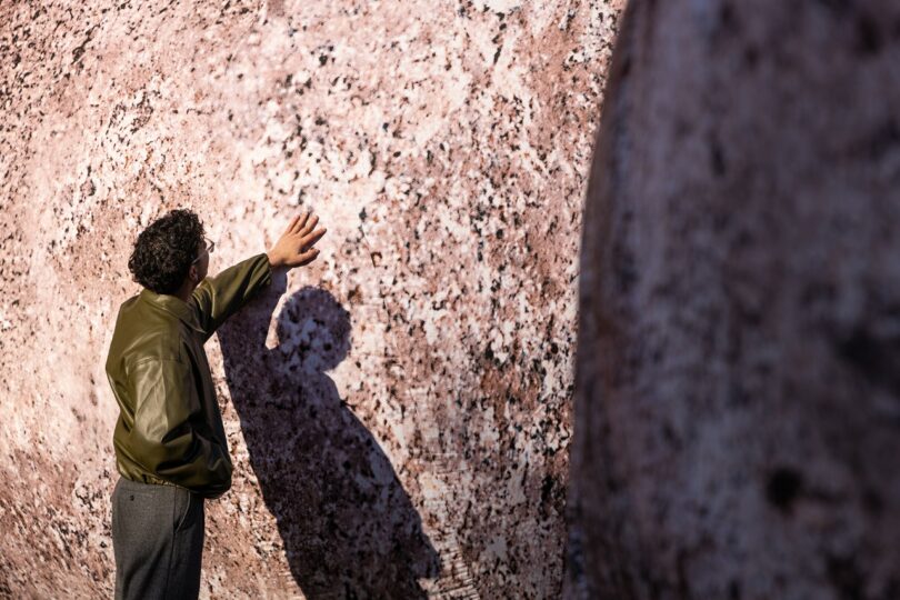 Close-up of a person in a green jacket touching the textured surface of an inflatable rock sculpture.
