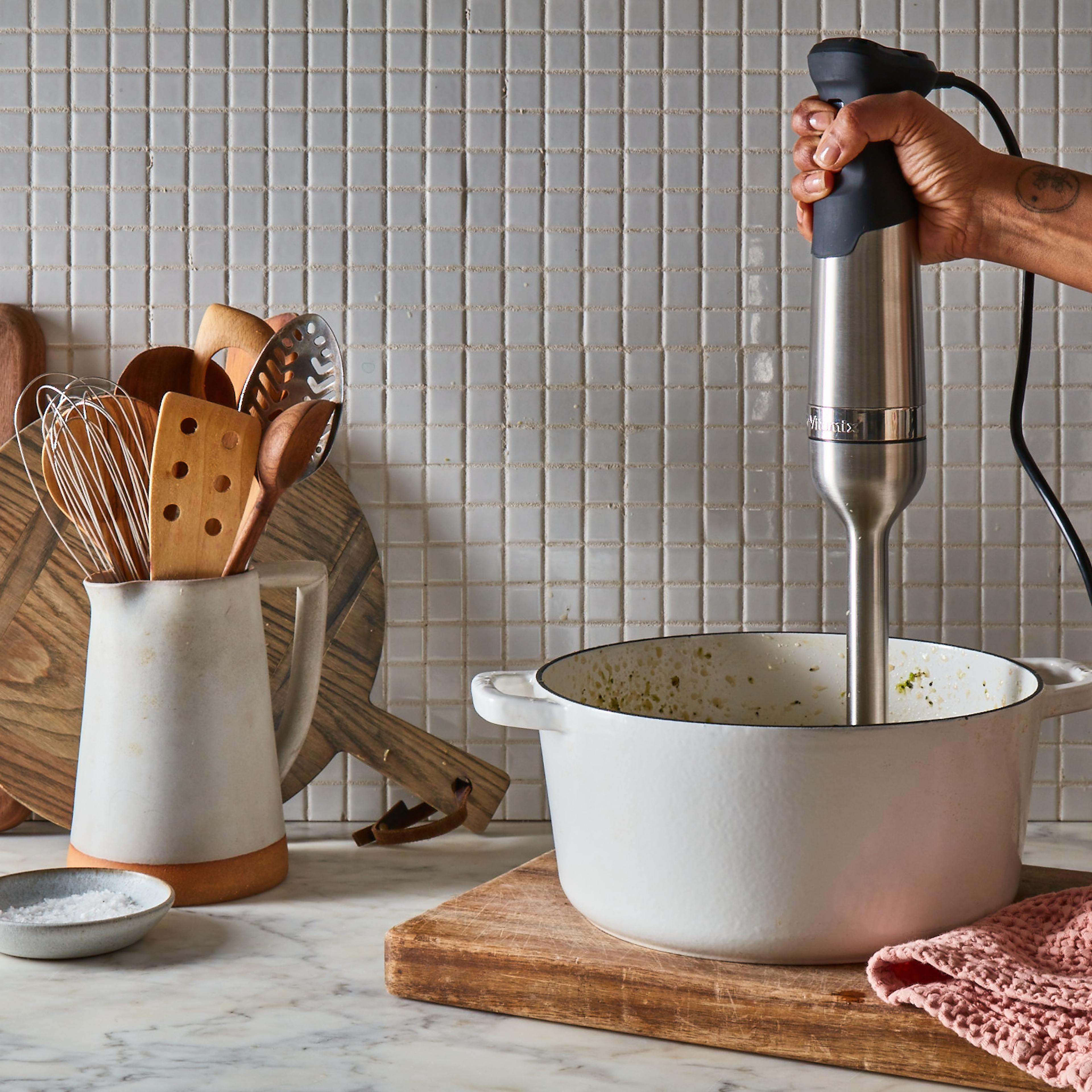 A hand-held immersion blender mixing a green smoothie directly in a glass bowl.