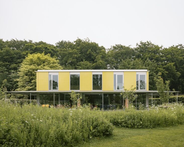 Exterior view of the modular industrial steel frame house clad in yellow and pale gray glazed tiles.
