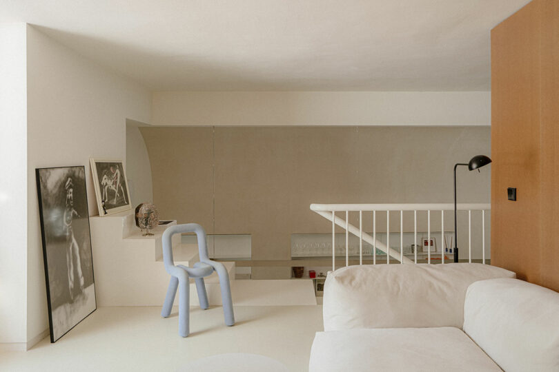 A minimalist loft interior viewed from above, featuring a blue chair and white sofa.