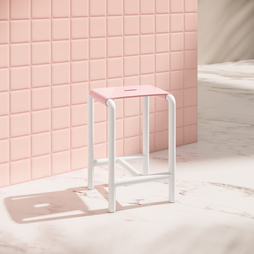 A pink and white stool on a marble floor next to a pink tiled wall.