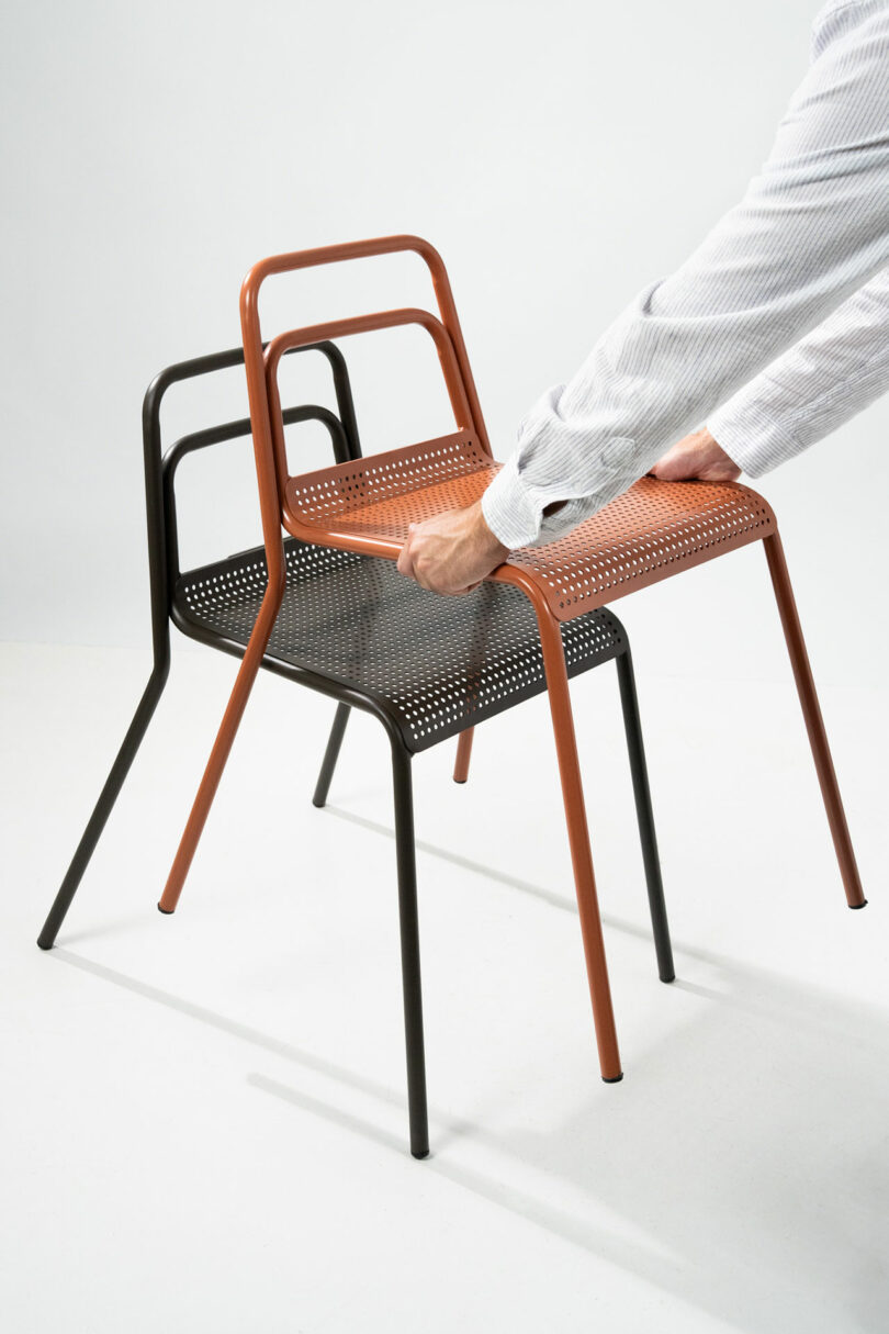 A person stacking a brown metal chair on top of a black one to demonstrate space-saving storage.