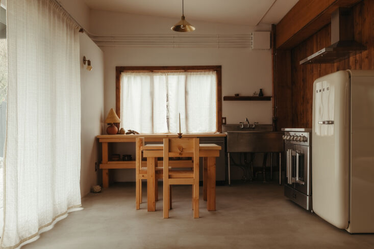 Interior view of a minimalist wooden kitchen featuring custom fir shelving and a dining table.