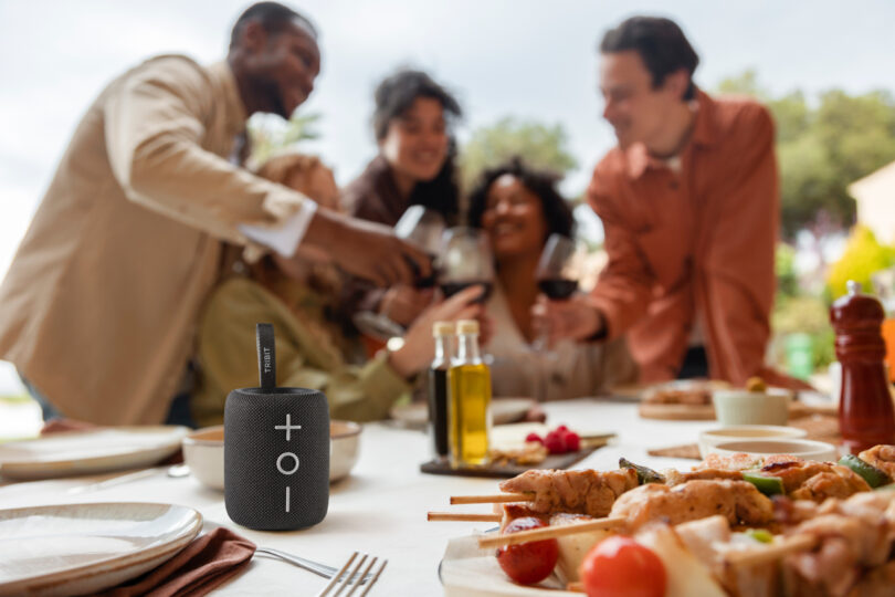 A TRIBIT speaker placed on an outdoor dining table during a small gathering of friends.