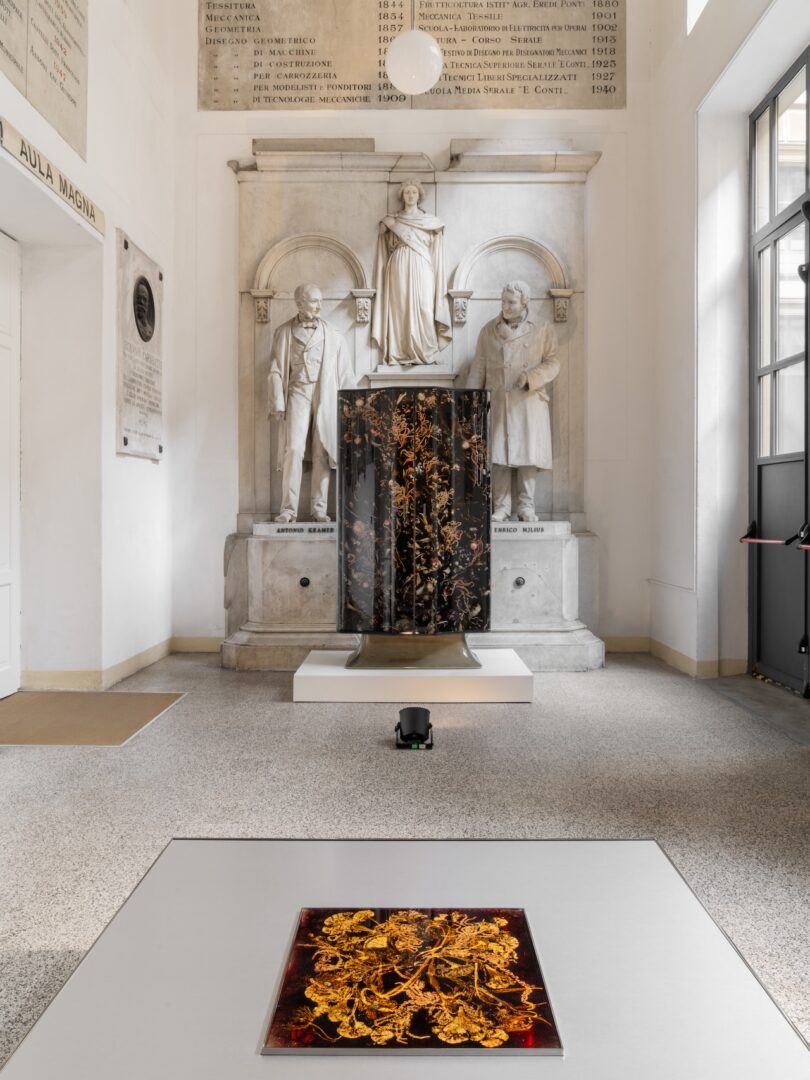 Two contemporary floral screens with intricate gold and black patterns displayed in a classical hall with marble statues.