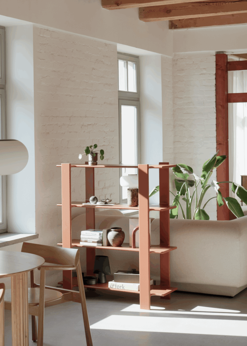 Modern living room with a red open bookshelf against a large window with sunlight streaming through.