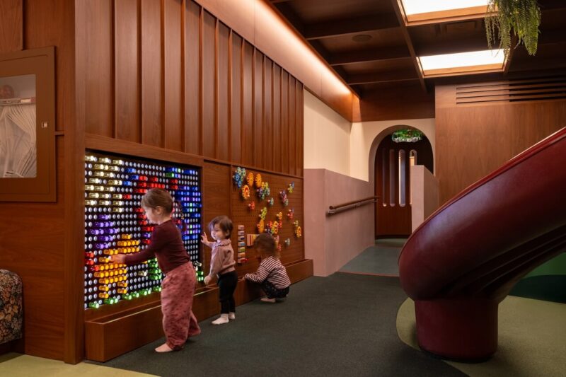 Children interacting with a large-scale Lite Brite style peg wall in a wood-paneled room.