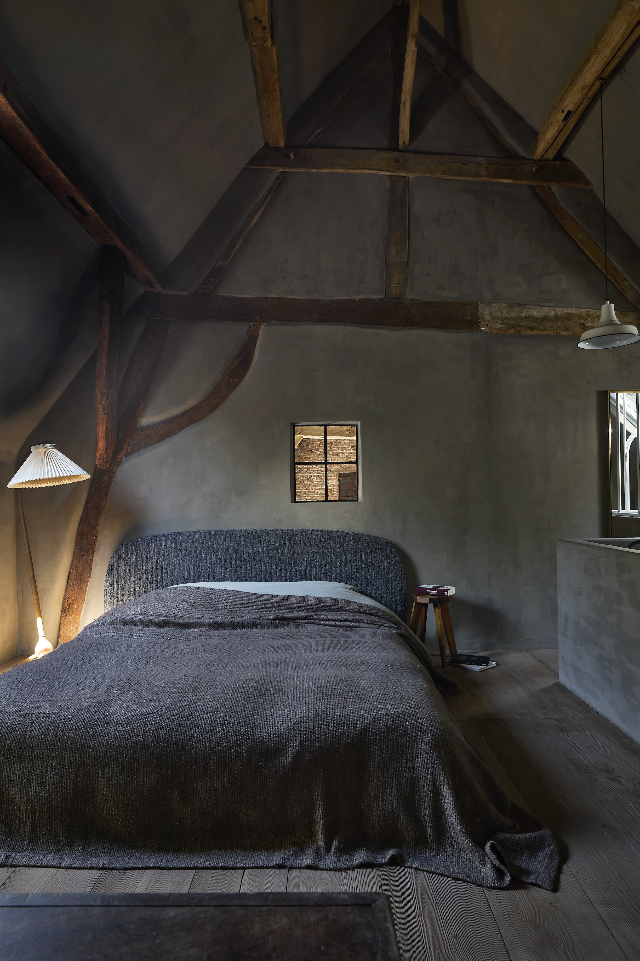 An attic bedroom with sloped ceilings, featuring a large wooden bed and vintage textiles.