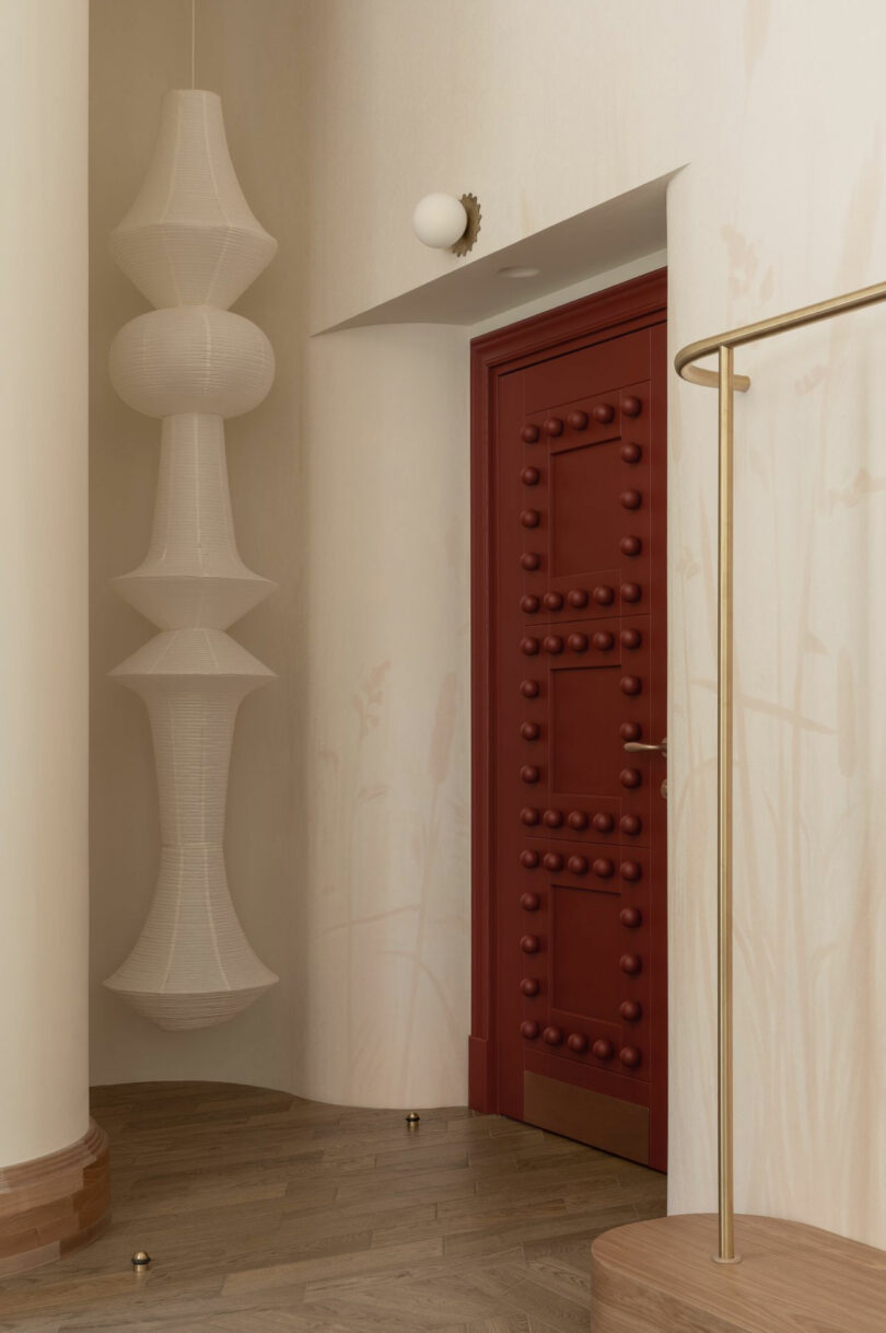 A luxury burgundy door with circular decorative handles next to a gold clothing rack.