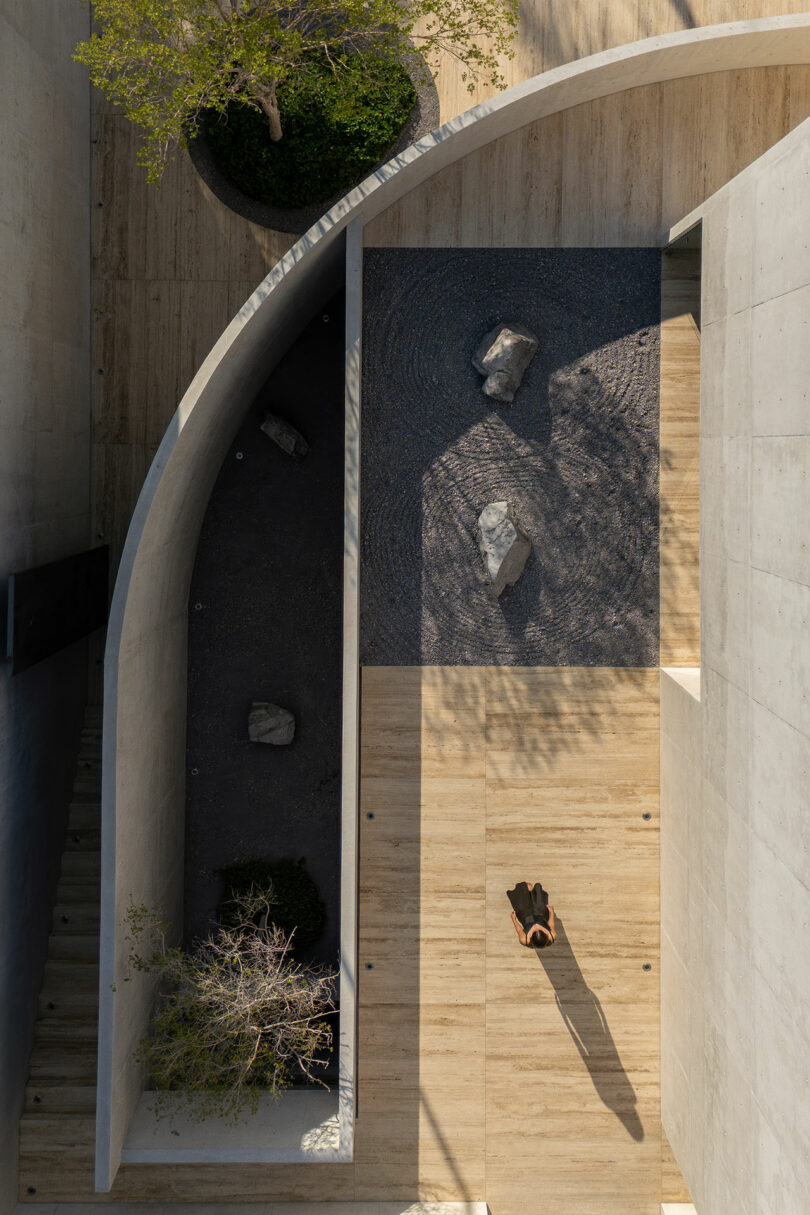 Top-down view of a person standing in a minimalist courtyard with gravel patterns, rocks, and wooden flooring.
