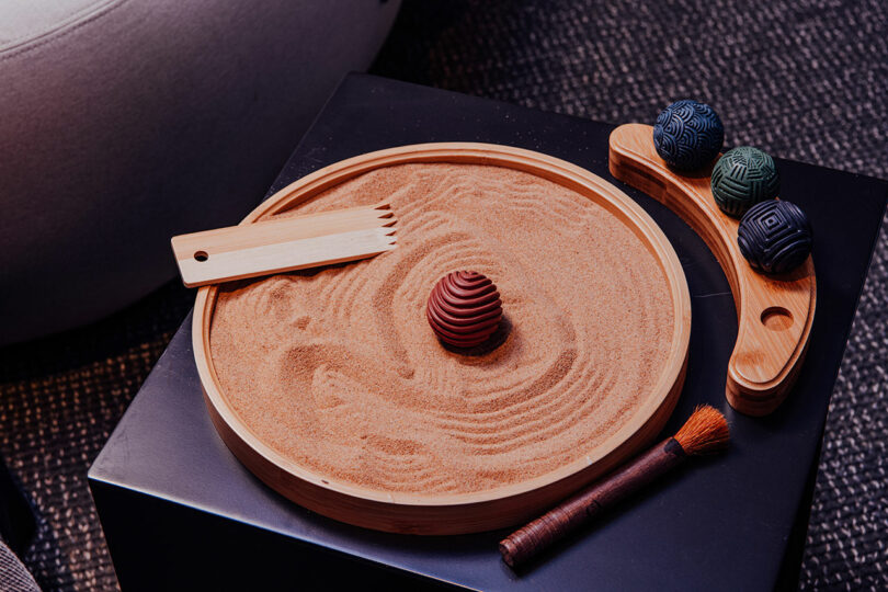 A close-up of a tabletop zen sand garden with a wooden rake and patterned stones.