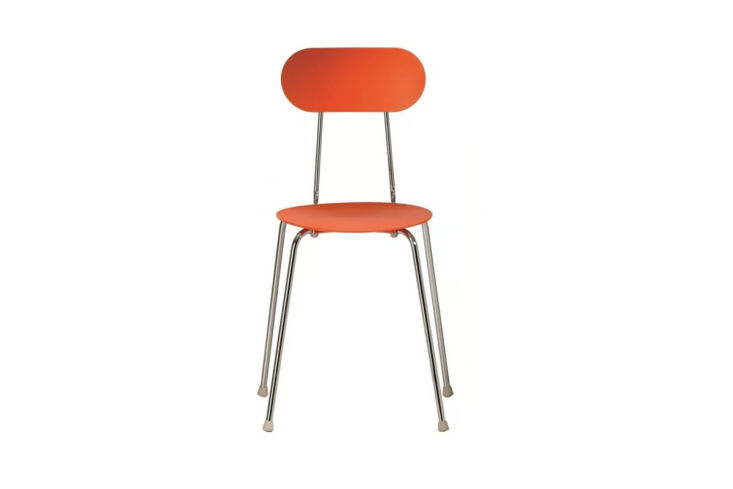 Bright orange Enzo Mari dining chairs tucked under a wooden dining table.