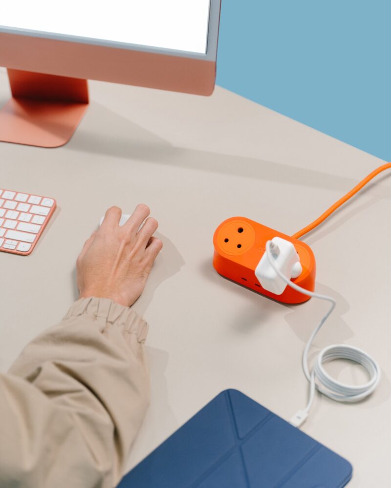 Close-up of a desktop setup featuring an orange power strip with a USB-C charging adapter and cable plugged in.