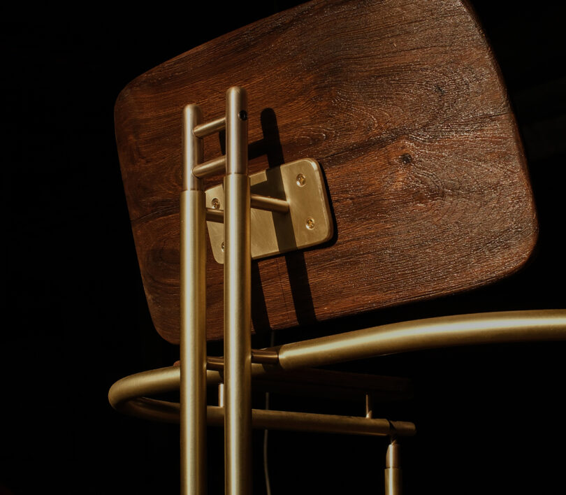 Close-up of a chair's backrest showing the intersection of polished gold-colored metal supports and solid wood.